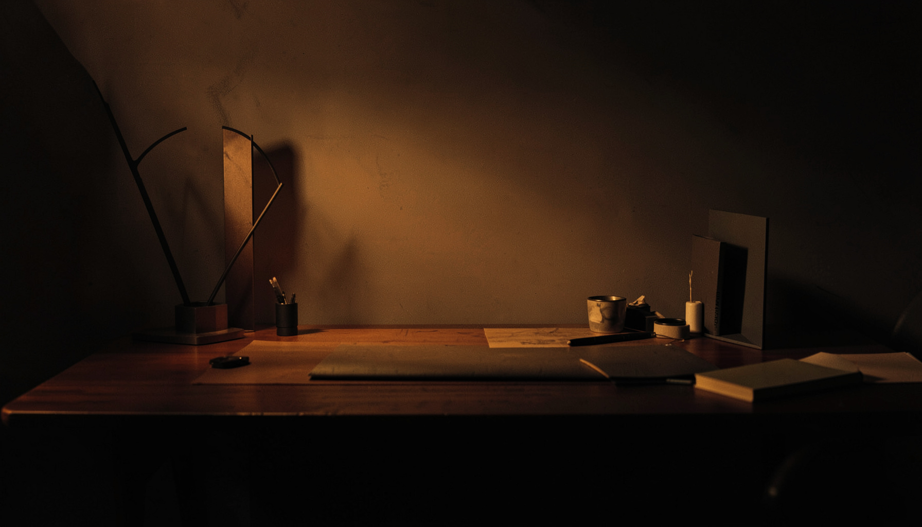 Dark abstract workspace with warm amber and charcoal tones, a designer's desk with subtle creative tools in shadow