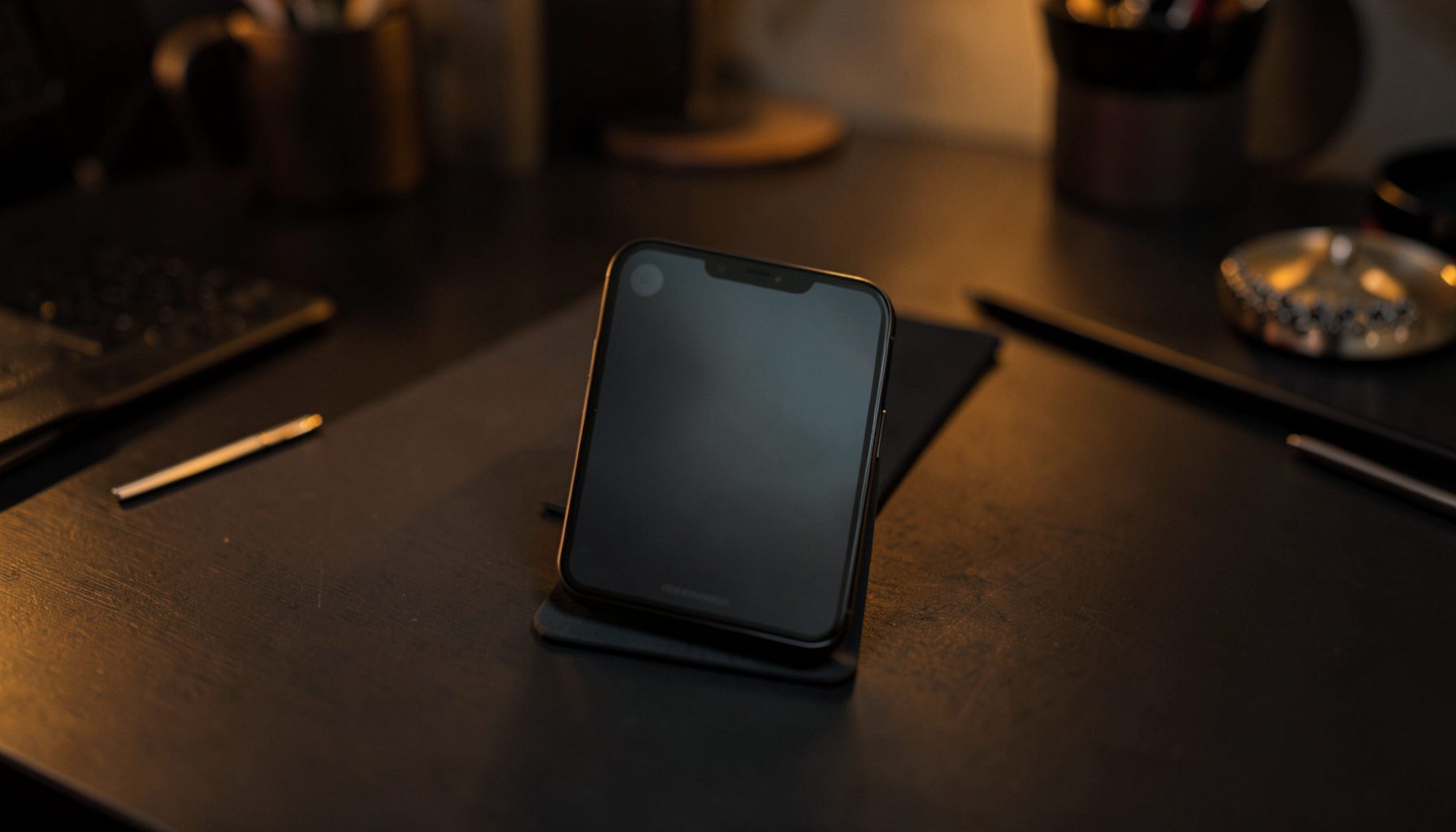 Sleek smartphone mockup displayed on a dark desk surface with warm amber and charcoal tones, moody creative workspace atmosphere